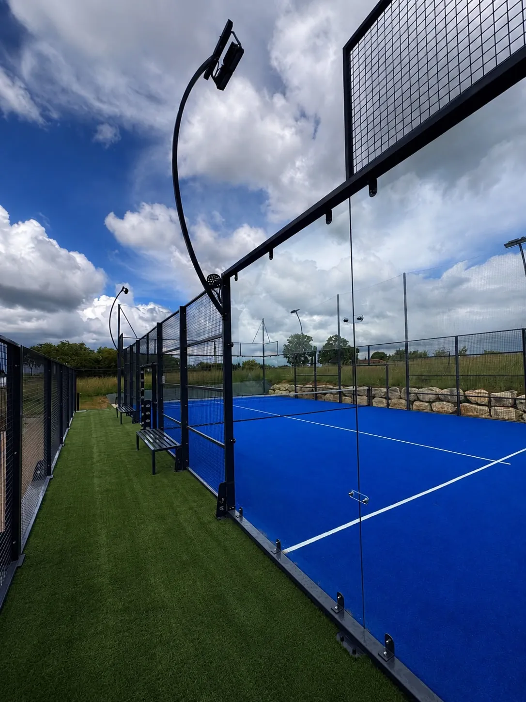 Panoramic glass entrance and curved lighting on a padel court in France